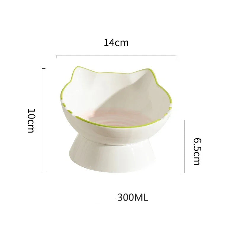 Fiche technique d'une gamelle pour chat en céramique blanche de 300 ml avec dimensions : 14 cm de large, 10 cm de haut et base surélevée à 6,5 cm. Cette gamelle chat surélevée au design de tête de chat avec liseré vert assure une hygiène parfaite et un confort ergonomique. Une gamelle robuste et élégante pour un repas sain.