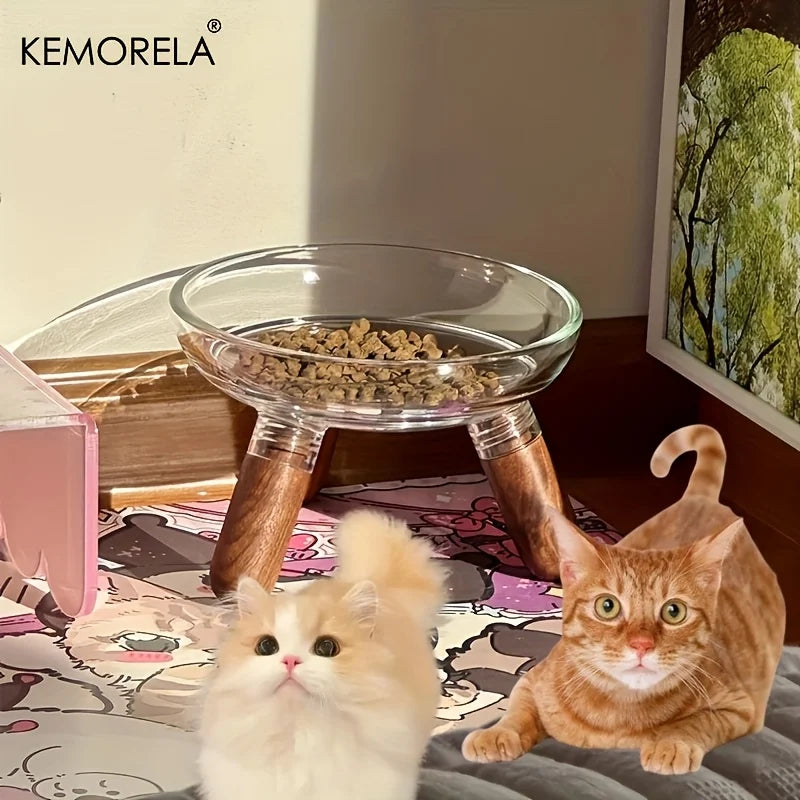 Gamelle surélevée Kemorela pour chat avec bol en verre transparent rempli de croquettes, support trépied en bois foncé élégant, présentée avec deux chats dans un intérieur moderne et lumineux.