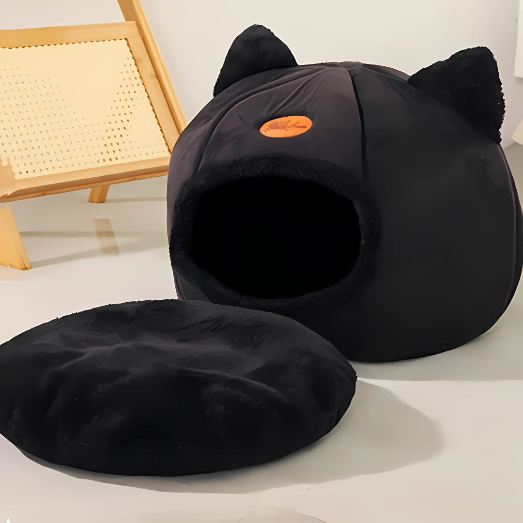 Niche pour chat fermée noire en forme d'igloo avec oreilles, montrant le coussin intérieur déhoussable et amovible pour un entretien facile, posée dans un intérieur moderne