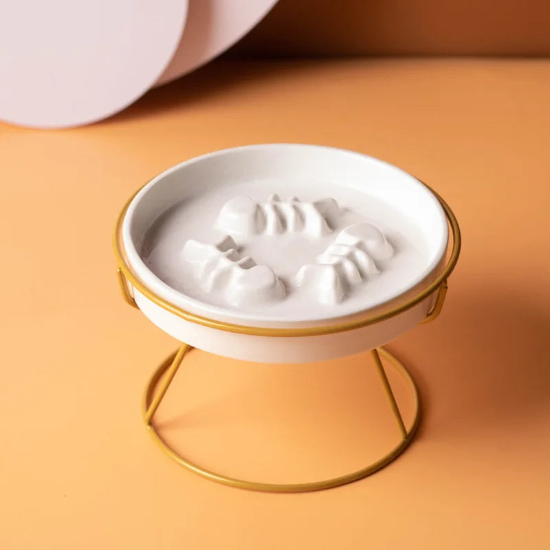 Plan rapproché montrant une gamelle anti-glouton pour chat en céramique blanche surélevée sur son support en métal doré. Le zoom met en évidence le labyrinthe intérieur en relief (arêtes de poisson), conçu comme un anti glouton chat efficace pour ralentir la prise de nourriture et améliorer la digestion. Solution santé et design disponible chez Les Trésors d'Owka.