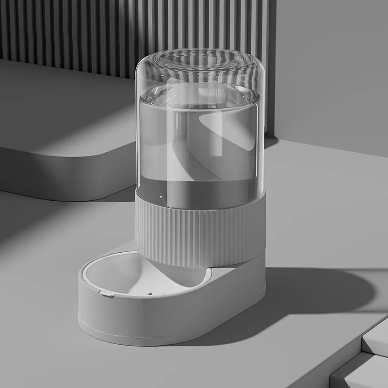 Vue de profil d'un abreuvoir automatique gris design assorti au distributeur croquettes chat de la collection. Le visuel montre le réservoir d'eau transparent par gravité et le socle texturé strié moderne. Cet abreuvoir complète parfaitement un distributeur croquettes pour une autonomie sans électricité. Idéal avec un distributeur croquettes chien miniature pour un coin repas urbain et épuré.