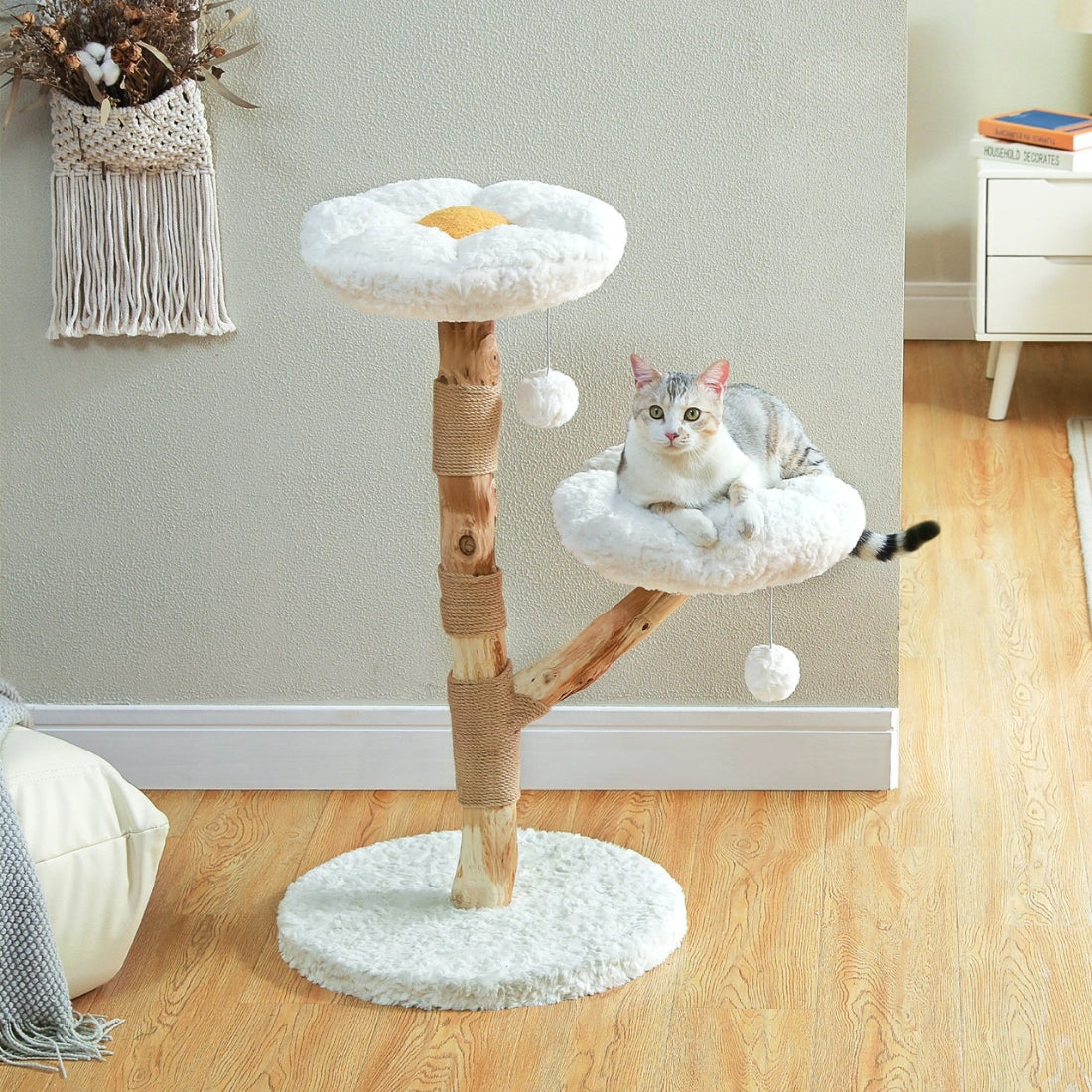 Arbre à chat design en bois naturel avec deux plateformes en forme de marguerites blanches, griffoir en corde de sisal et pompons suspendus, idéal pour une décoration d'intérieur zen.