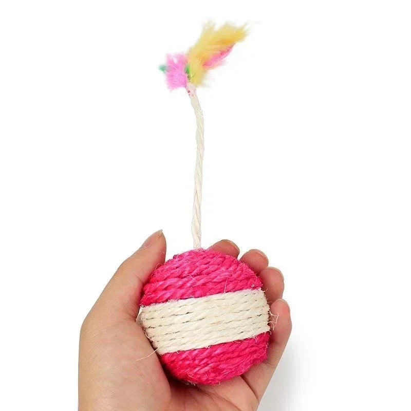 Balle pour chat en sisal naturel tressé de couleur rose et blanc, tenue à la main pour montrer sa taille, surmontée d'une tige flexible avec des plumes multicolores.