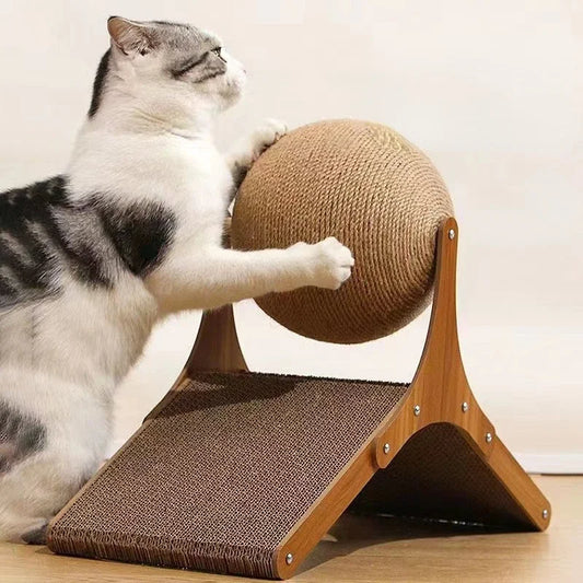 Chat blanc et gris utilisant une station de griffage interactive comprenant une grande balle rotative en sisal et une base triangulaire en bois avec tunnel en carton ondulé.