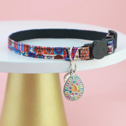 Bijou de cou pour chat au motif mosaïque rouge et bleu, présenté sur un support doré, avec un pendentif mandala goutte nacrée multicolore et un fermoir de sécurité noir.