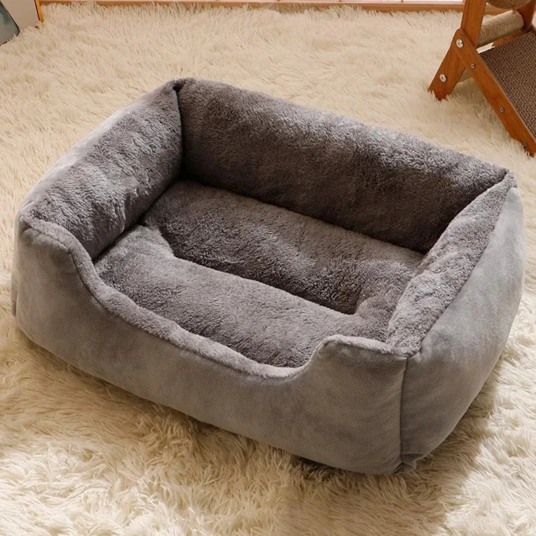 Canapé pour chat rectangulaire gris avec bords surélevés protecteurs, extérieur en velours résistant et intérieur en peluche grise ultra-douce, posé sur un tapis blanc.