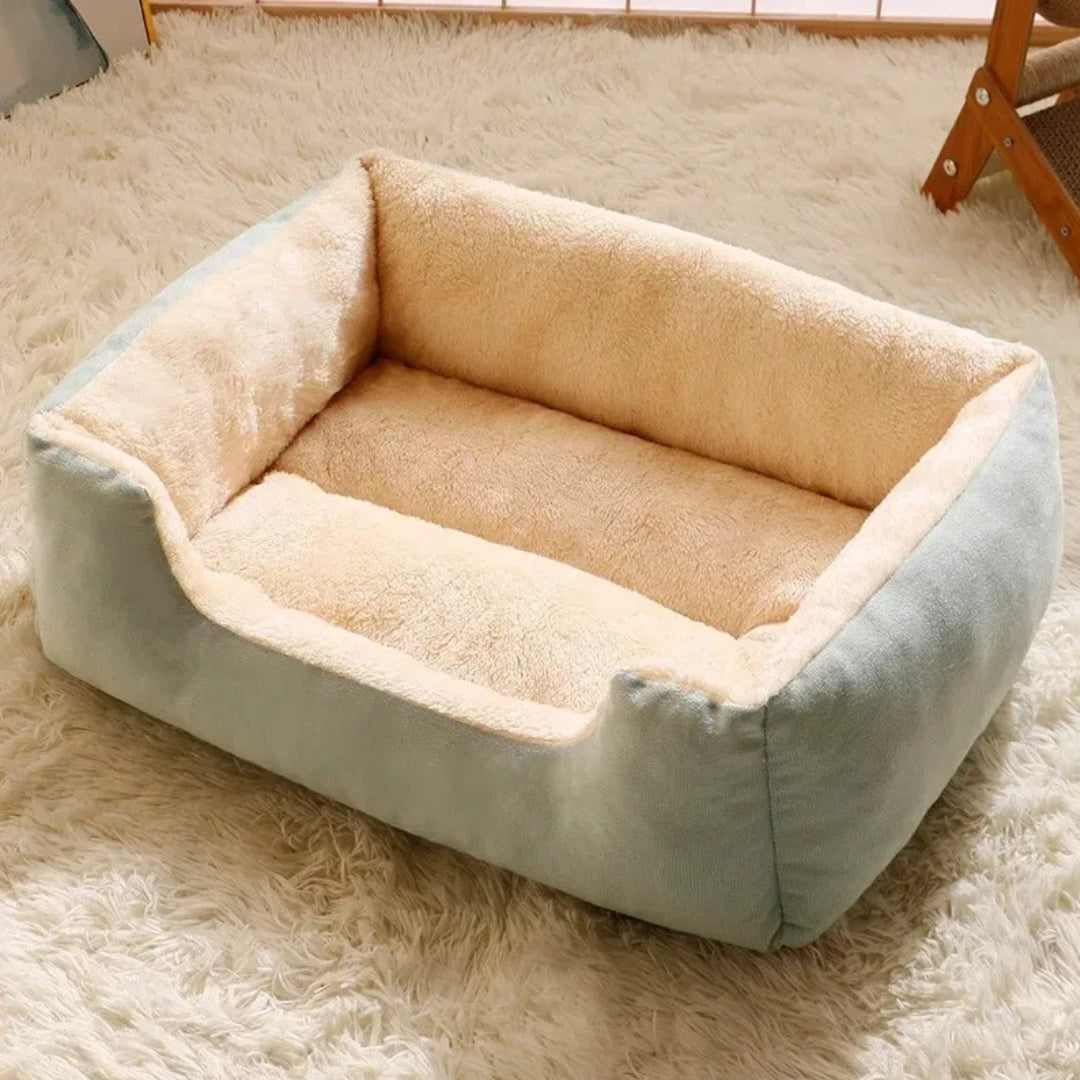 Canapé pour chat rectangulaire avec bords surélevés, extérieur en velours vert d'eau et intérieur en peluche beige ultra-douce, posé sur un tapis en fourrure blanche.
