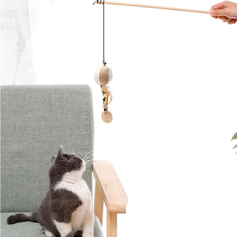Canne à pêche pour chat avec manche long en bois naturel, dotée d'un jouet suspendu en sisal blanc et beige avec plumes, présentée face à un chat gris et blanc attentif.