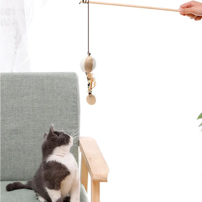 Canne à pêche pour chat avec manche long en bois naturel, dotée d'un jouet suspendu en sisal blanc et beige avec plumes, présentée face à un chat gris et blanc attentif.