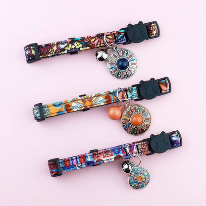 Vue de dessus de trois colliers pour chats aux motifs ethniques variés, ornés de médaillons mandala colorés, de clochettes sonores et de fermoirs de sécurité noirs en forme de tête de chat.