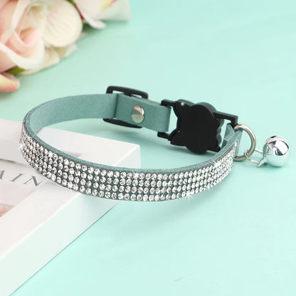Collier pour chat en velours bleu menthe orné de trois rangées de strass étincelants, avec boucle de sécurité noire et grelot argenté posé sur un support élégant.