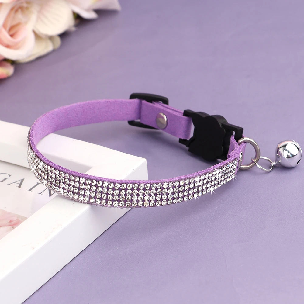 Collier pour chat en velours violet orné de trois rangées de strass étincelants, avec boucle de sécurité noire et grelot argenté posé sur un support élégant.