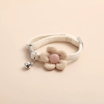 Collier pour chat crème en tissu ultra-doux orné d'une grande fleur en tricot beige et rose poudré. Vue d'un collier chaton ajustable muni d'une clochette argentée et d'une boucle de sécurité grise. Accessoire confortable style kawaii bohème pour collier chat. Les Trésors d'Owka.