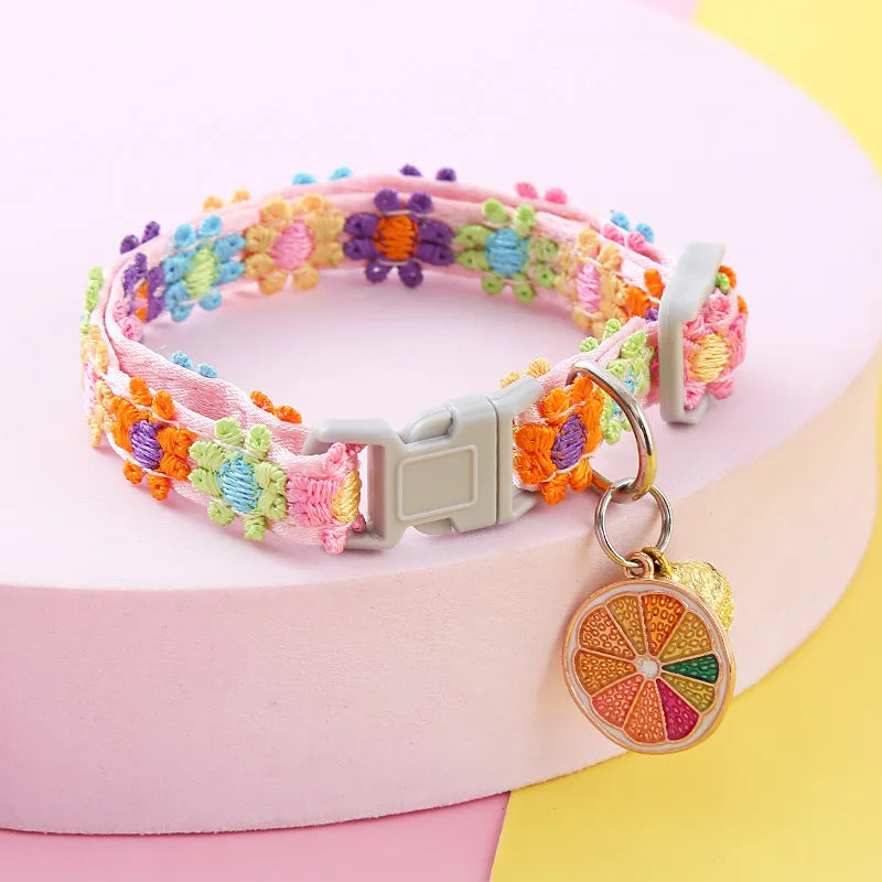 Collier pour chat rose avec broderie de fleurs multicolores en relief. Ce collier chaton ajustable possède un pendentif original en forme de tranche d'orange et un grelot doré. Accessoire de style bohème coloré pour collier chat, idéal pour un look estival et unique. Haute qualité Les Trésors d'Owka.