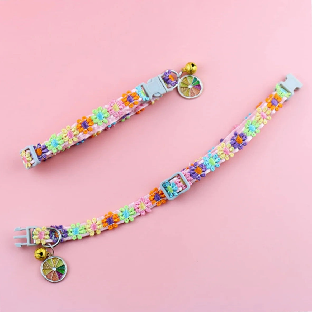Vue à plat de deux colliers pour chat roses aux fleurs brodées multicolores. L'image montre le collier ouvert avec sa boucle réglable, son grelot doré et son pendentif tranche d'orange. Collier chaton ajustable au design bohème, conçu avec des finitions de haute qualité. Accessoire sécurisé pour collier chat. Les Trésors d'Owka.