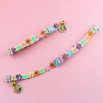Vue à plat de deux colliers pour chat roses aux fleurs brodées multicolores. L'image montre le collier ouvert avec sa boucle réglable, son grelot doré et son pendentif tranche d'orange. Collier chaton ajustable au design bohème, conçu avec des finitions de haute qualité. Accessoire sécurisé pour collier chat. Les Trésors d'Owka.
