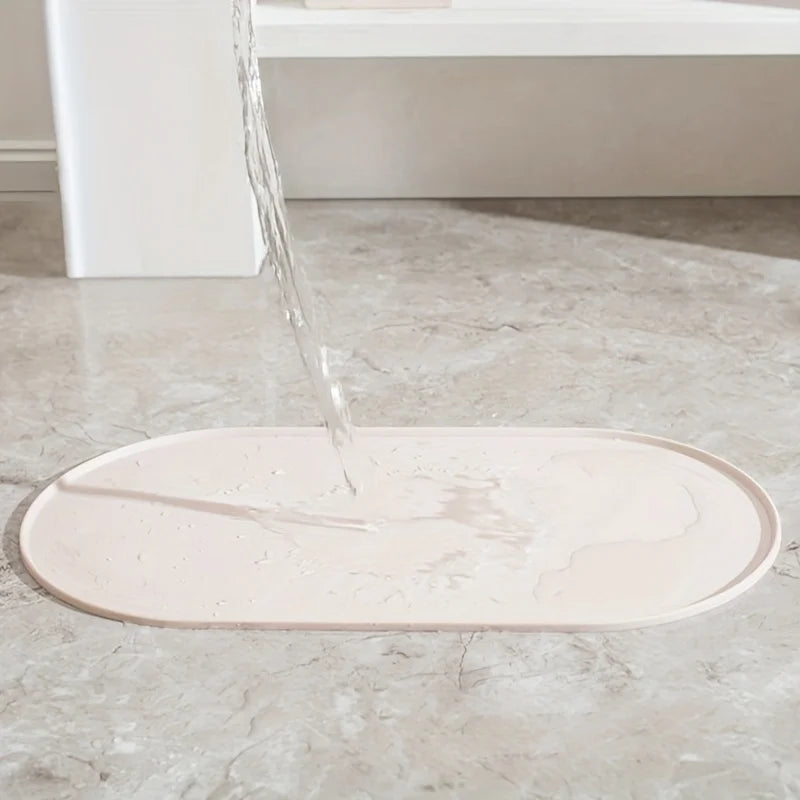 Démonstration de l'étanchéité totale d'un tapis gamelles chat ovale en silicone beige de la marque Les Trésors d'Owka. L'image montre de l'eau versée sur le tapis chat, illustrant l'efficacité de ses bords surélevés anti-débordement qui retiennent les liquides pour protéger vos sols de l'humidité et des taches. Ce tapis gamelles de haute qualité, posé sur un sol en marbre, offre une barrière imperméable et antidérapante idéale pour le coin repas de votre animal. Fabriqué en silicone alimentaire durable et f