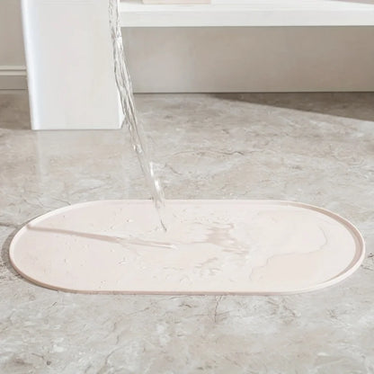 Démonstration de l'étanchéité totale d'un tapis gamelles chat ovale en silicone beige de la marque Les Trésors d'Owka. L'image montre de l'eau versée sur le tapis chat, illustrant l'efficacité de ses bords surélevés anti-débordement qui retiennent les liquides pour protéger vos sols de l'humidité et des taches. Ce tapis gamelles de haute qualité, posé sur un sol en marbre, offre une barrière imperméable et antidérapante idéale pour le coin repas de votre animal. Fabriqué en silicone alimentaire durable et f