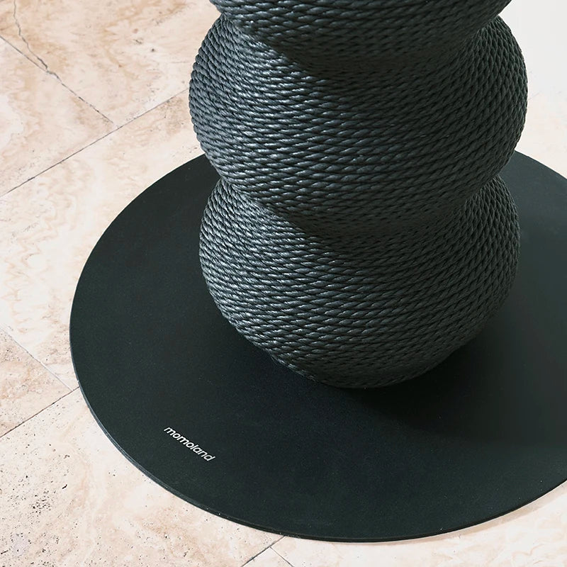 Gros plan sur la base circulaire noire lestée et le tissage serré en corde haute densité d'un poteau à griffer sculptural Momoland pour chat.