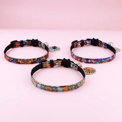 Gros plan sur trois colliers pour chats aux motifs ethniques vibrants, ornés de médaillons mandala colorés, de clochettes argentées et de fermoirs de sécurité noirs en forme de tête de chat.