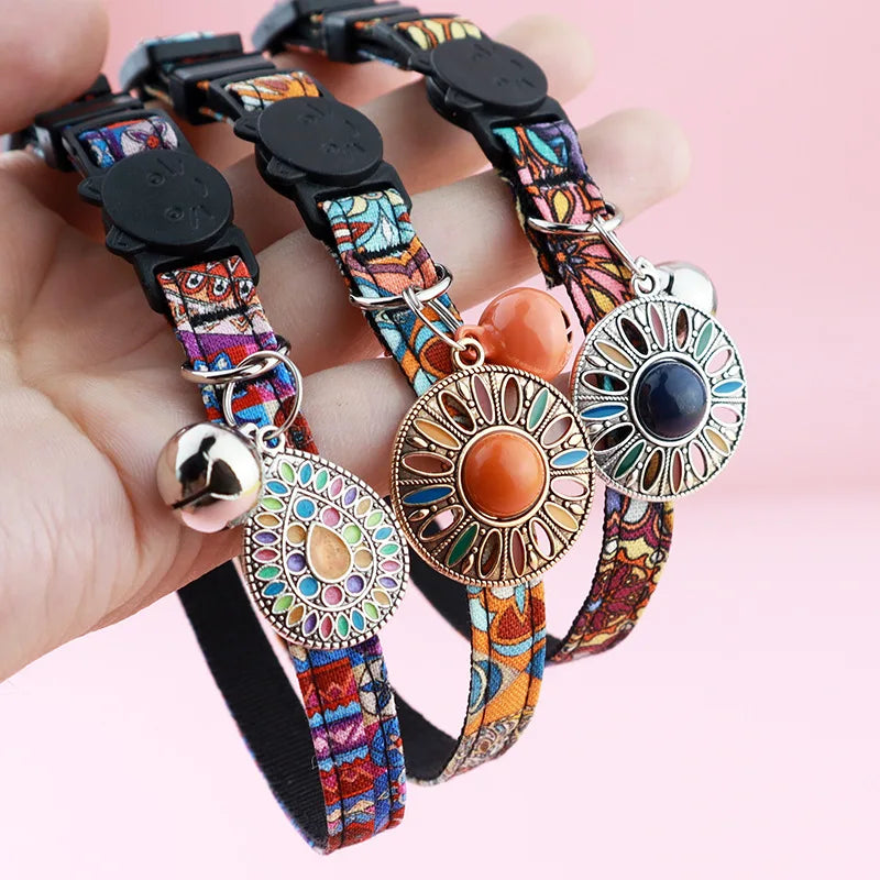 Gros plan sur trois colliers pour chats aux motifs ethniques vibrants, ornés de médaillons mandala colorés, de clochettes argentées et de fermoirs de sécurité noirs en forme de tête de chat.
