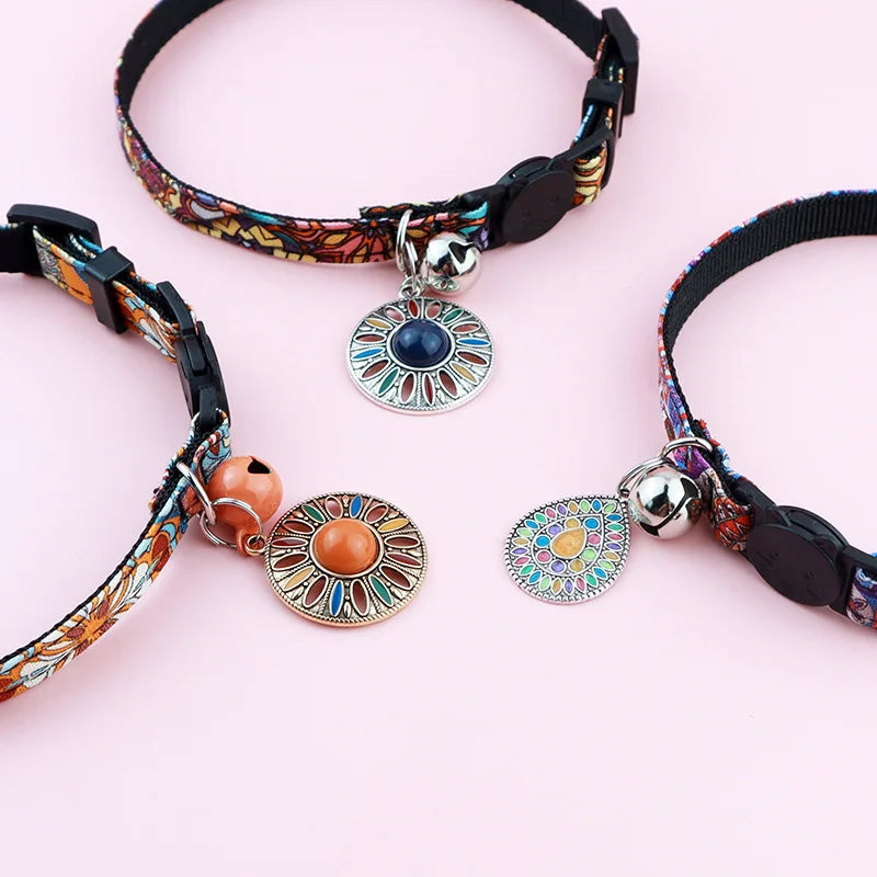 Gros plan sur trois colliers pour chats aux motifs ethniques vibrants, ornés de médaillons mandala colorés, de clochettes argentées et cuivrées, et de fermoirs de sécurité noirs.