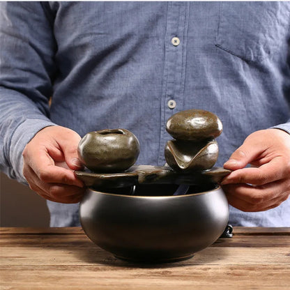 Personne tenant les composants d'une fontaine zen artisanale montrant sa taille compacte, avec un bassin circulaire en céramique noire et des éléments d'écoulement texturés.