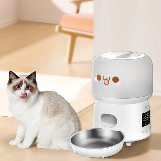 Distributeur automatique de croquettes blanc au design mignon avec visage souriant, écran LCD de programmation et bol en acier inoxydable, présenté à côté d'un chat Ragdoll.