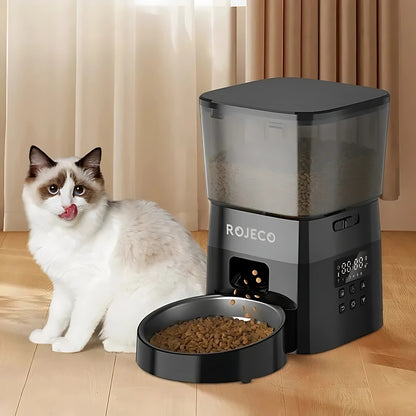Distributeur automatique de croquettes ROJECO noir avec réservoir transparent et écran de programmation LED, montrant la distribution de nourriture dans un bol en acier inoxydable devant un chat Ragdoll.