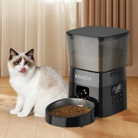 Distributeur automatique de croquettes ROJECO noir avec réservoir transparent et écran de programmation LED, montrant la distribution de nourriture dans un bol en acier inoxydable devant un chat Ragdoll.