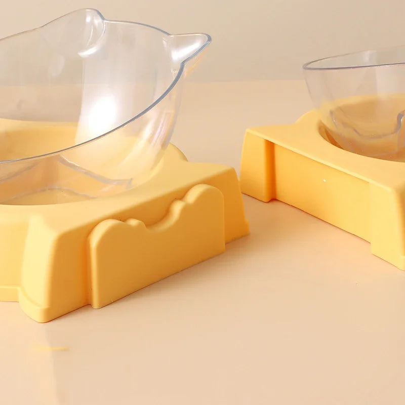 Gros plan sur un distributeur croquettes chat orthopédique avec bol transparent incliné à 15 degrés sur socle jaune. Le visuel montre la finition premium et l'ergonomie du produit. Ce distributeur croquettes manuel est conçu pour le confort cervical des animaux. Parfait comme distributeur croquettes chien de petite taille pour faciliter la digestion.