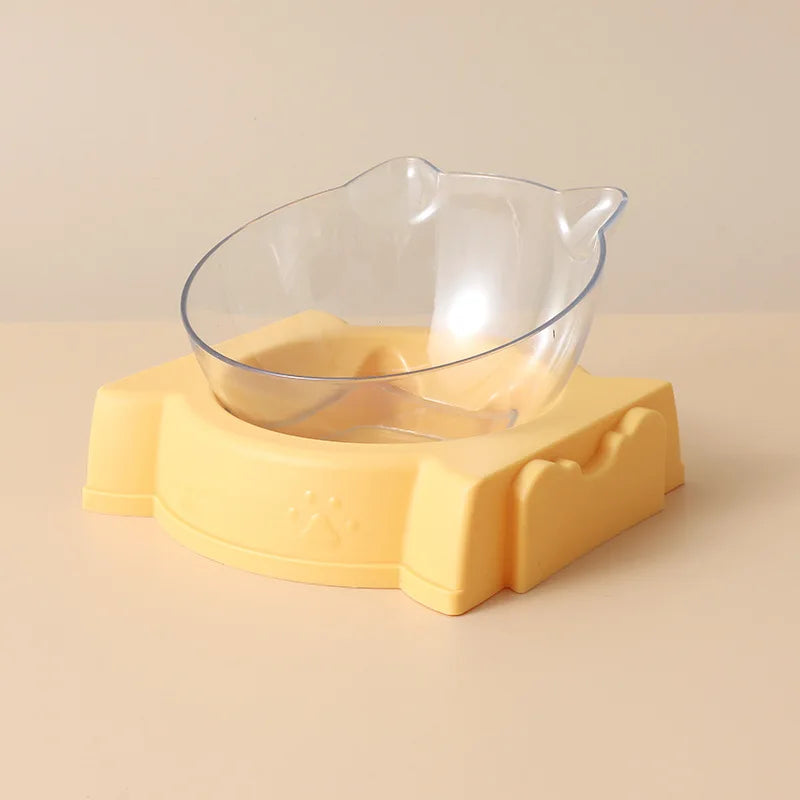 Vue de profil d'un distributeur croquettes chat orthopédique composé d'un bol transparent incliné avec oreilles de chat sur un socle jaune pastel. Le visuel montre l'inclinaison ergonomique pour le confort cervical. Ce distributeur croquettes manuel est idéal pour prévenir les reflux. Parfait comme distributeur croquettes chien miniature pour une alimentation saine et design.