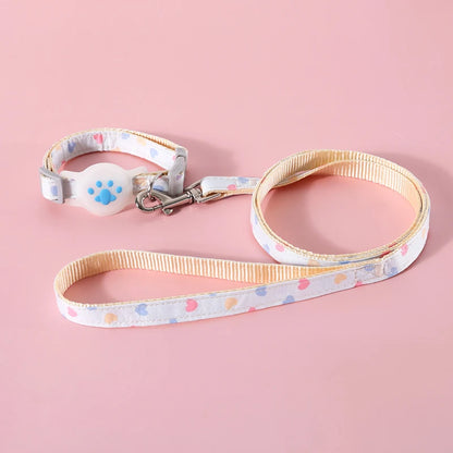 Ensemble collier gps pour chat et laisse assortie blancs à motifs cœurs pastels. Support AirTag en silicone blanc avec patte bleue en relief. Ce collier gps chat réglable est relié à une laisse robuste par un mousqueton métallique chromé. Solution complète type collier gps à chat pour des promenades sécurisées, alliant design Kawaii et confort.