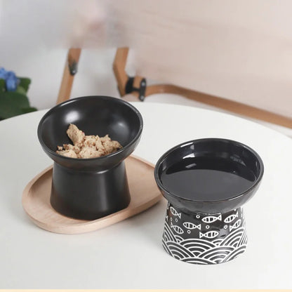 Duo de gamelle pour chat surélevée en céramique noire comprenant un bol à nourriture uni et un bol à eau motif japonais poisson, sur plateau en bois. Cette gamelle chat orthopédique haut de gamme assure une posture de repas naturelle et une hygiène parfaite. Une gamelle de luxe stable et élégante pour un coin repas zen.