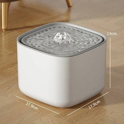 Fontaine à eau pour chat carrée blanche avec dimensions : 17,9 cm de largeur par 13 cm de hauteur, jet d'eau central bouillonnant et design épuré sur sol en parquet.