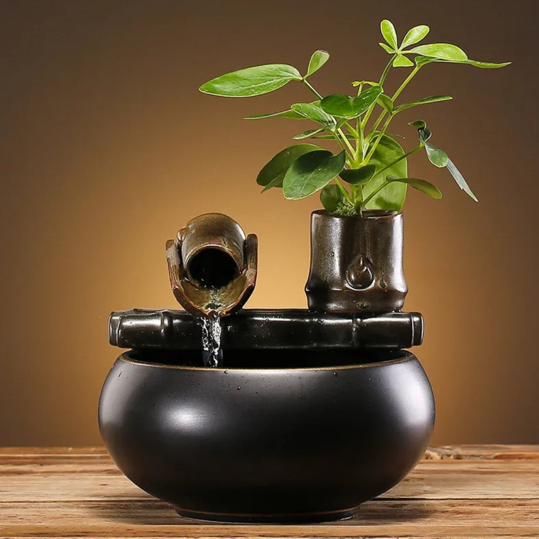 Fontaine d'intérieur zen en céramique noire satinée avec écoulement d'eau en bambou artificiel et petit pot de fleurs intégré contenant une plante verte décorative.