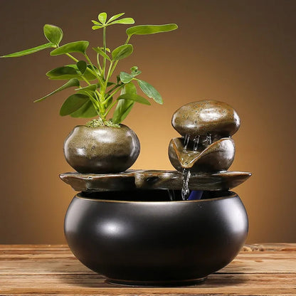 Fontaine zen d'intérieur avec cascade d'eau sur galets polis, pot en céramique avec plante verte et base circulaire noire mate élégante.