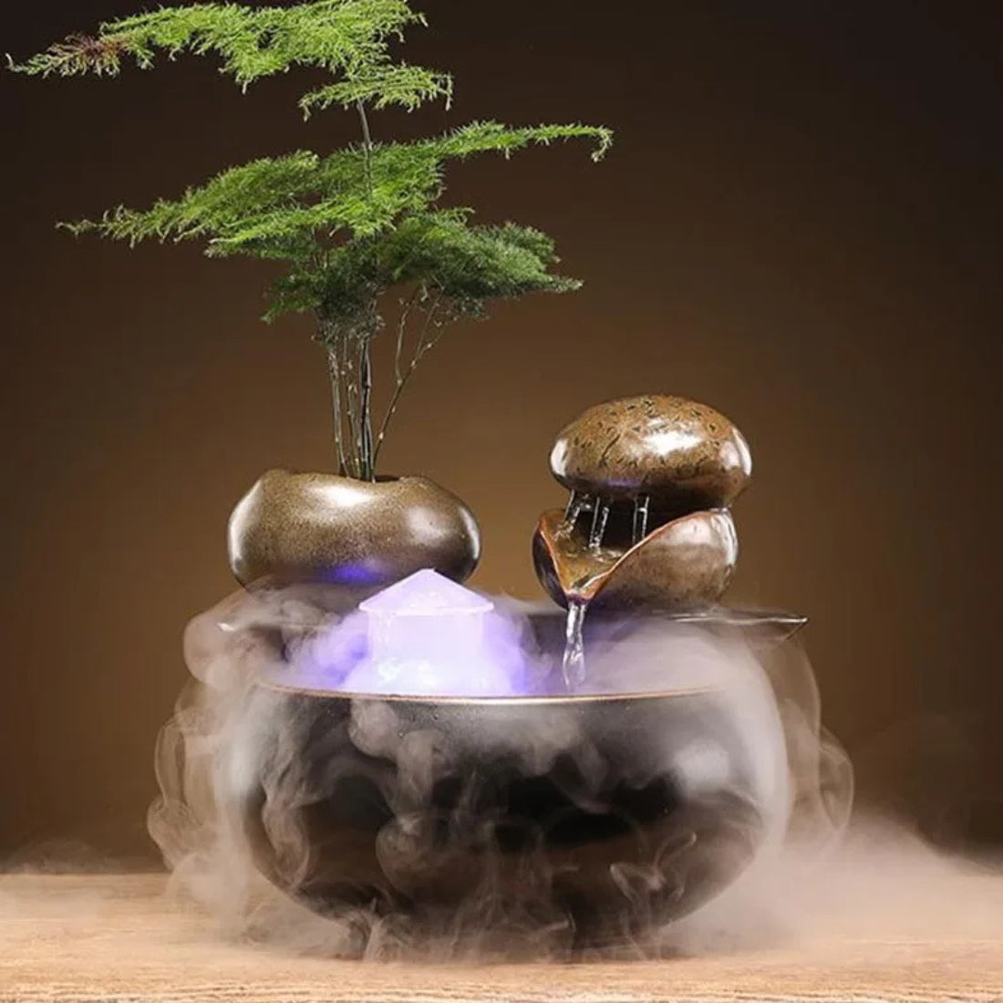 Fontaine zen d'intérieur en céramique avec cascade d'eau sur galets, brumisateur ultrasonique générant une brume épaisse, lumière LED violette et support pour plante naturelle.