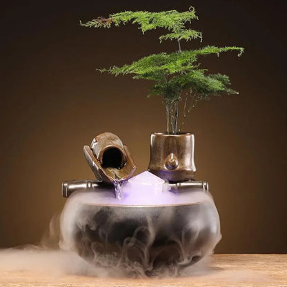 Fontaine zen en céramique avec brumisateur ultrasonique créant une fumée mystique, lumière LED intégrée et pot avec plante verte sur socle en bambou artificiel.