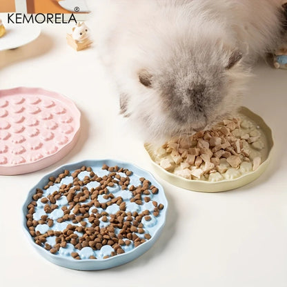 Démonstration d'utilisation de la gamelle anti glouton chat en céramique Kemorela. La photo montre une paire de mains tenant une gamelle glouton couleur crème remplie de morceaux de viande fraîche, prouvant sa compatibilité avec l'alimentation humide. À côté, une gamelle anti glouton rose contient des croquettes sèches, et une gamelle vert pastel vide met en évidence le motif de patte de chat en relief conçu pour ralentir la prise alimentaire. En bas à droite, une gamelle bleu pastel est partiellement visib