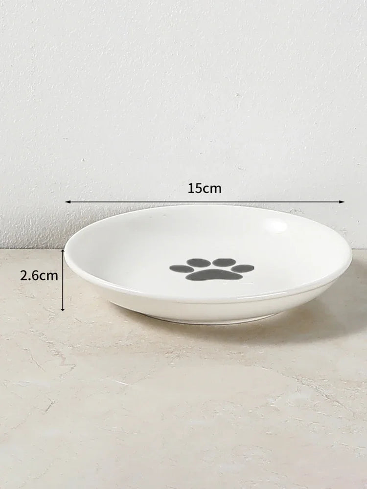 Gamelle pour chat en céramique blanche de 15 cm de diamètre et 2,6 cm de profondeur, avec motif patte de chat grise au centre, idéale pour prévenir la fatigue des moustaches.