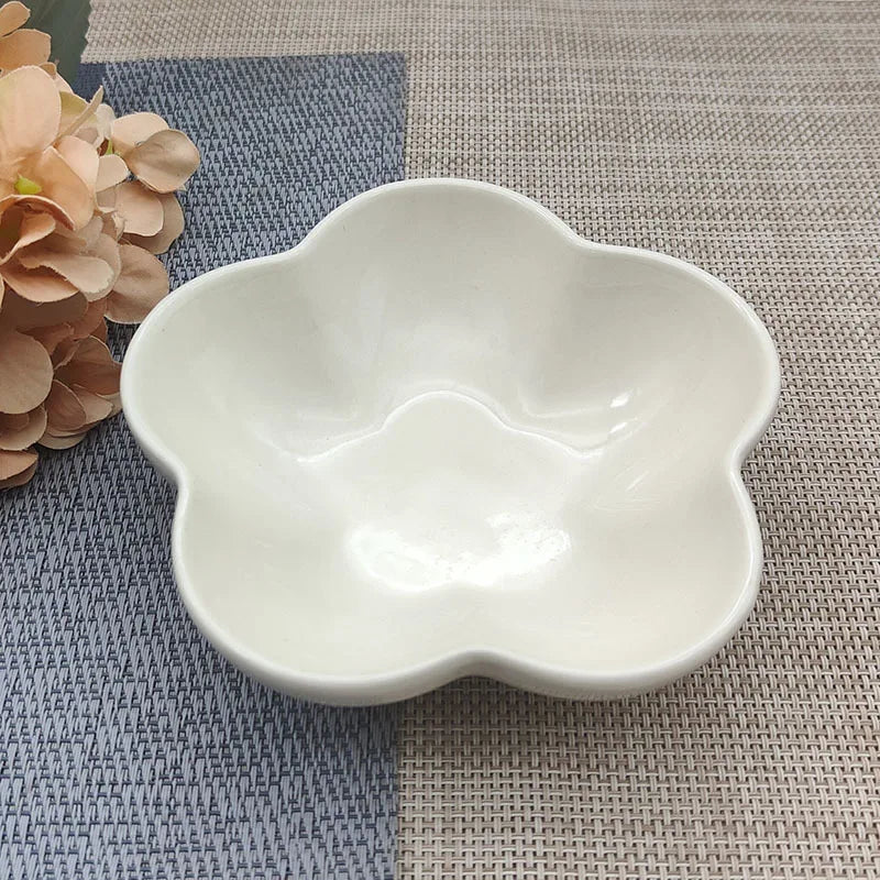Gamelle pour chat en céramique blanche brillante en forme de fleur, design évasé et peu profond pour prévenir la fatigue des moustaches, présentée sur un tapis de table texturé.