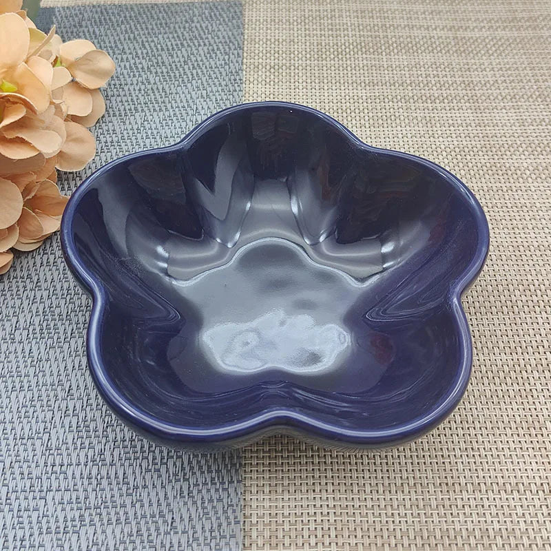 Gamelle pour chat en céramique bleu marine brillant en forme de fleur, design évasé et peu profond pour prévenir la fatigue des moustaches, présentée sur un tapis de table texturé.