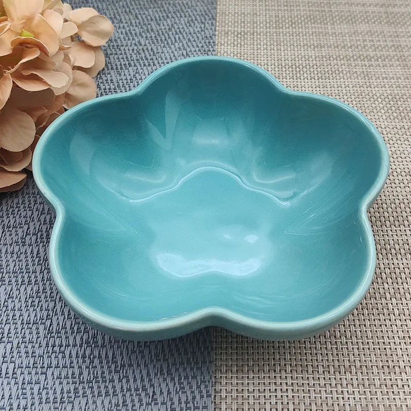 Gamelle pour chat en céramique bleu turquoise brillant en forme de fleur, design évasé et peu profond pour prévenir la fatigue des moustaches, présentée sur un tapis de table texturé.