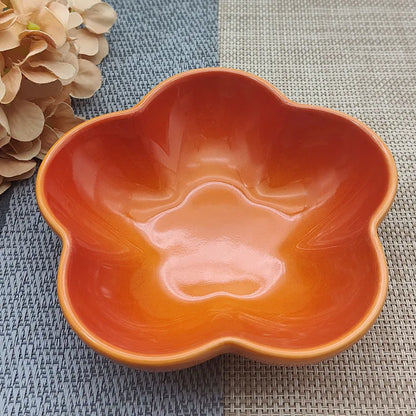 Gamelle pour chat en céramique orange corail brillant en forme de fleur, design évasé et peu profond pour prévenir la fatigue des moustaches, présentée sur un tapis de table texturé.