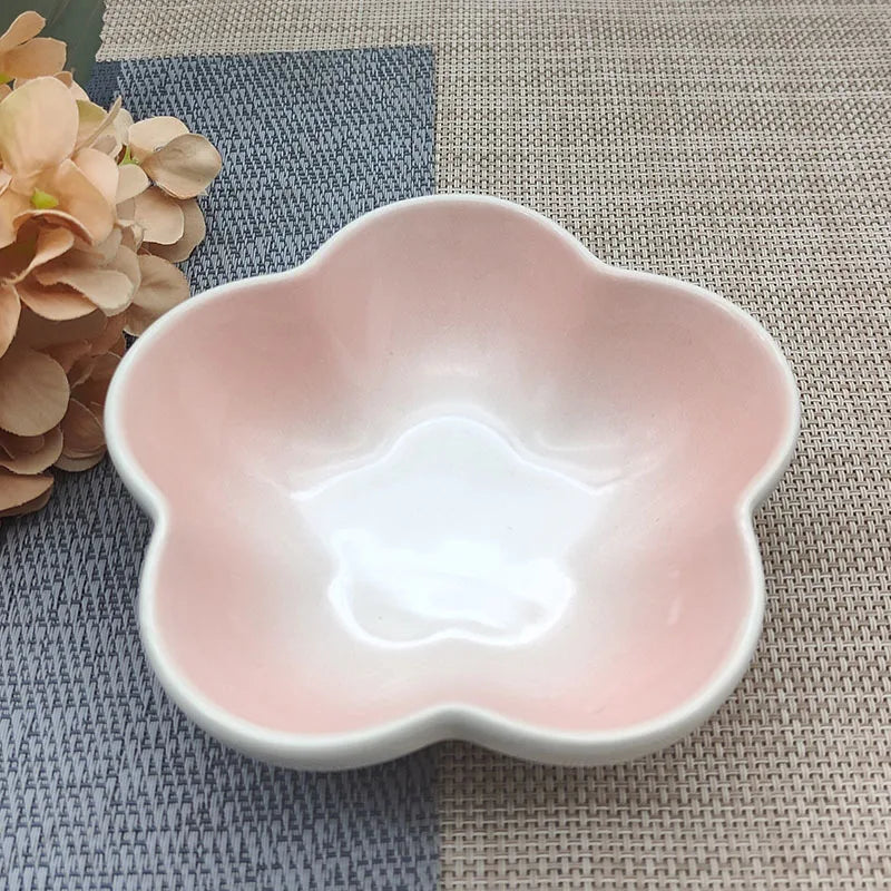 Gamelle pour chat en céramique avec dégradé rose et blanc en forme de fleur, design peu profond pour le confort des moustaches, posée sur un tapis de table bicolore.