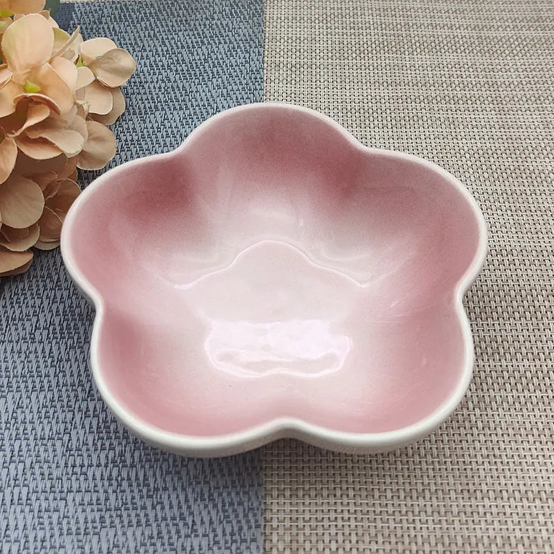 Gamelle pour chat en céramique rose pastel brillant en forme de fleur, design évasé et peu profond pour prévenir la fatigue des moustaches, présentée sur un tapis de table bicolore.