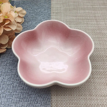 Gamelle pour chat en céramique rose pastel brillant en forme de fleur, design évasé et peu profond pour prévenir la fatigue des moustaches, présentée sur un tapis de table bicolore.