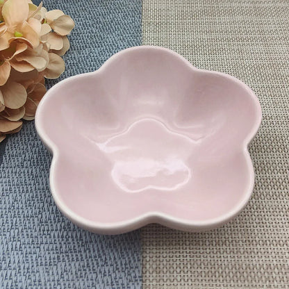Gamelle pour chat en céramique rose pastel brillant en forme de fleur, design évasé et peu profond pour prévenir la fatigue des moustaches, présentée sur un tapis de table bicolore.