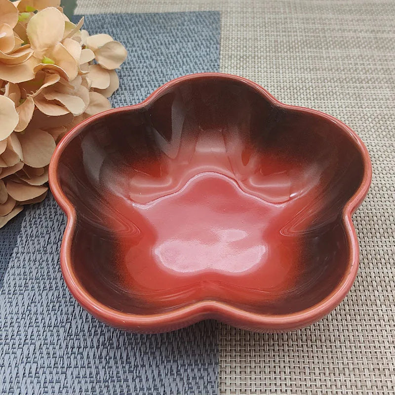 Gamelle pour chat en céramique rouge avec dégradé sombre en forme de fleur, design évasé et peu profond pour prévenir la fatigue des moustaches, présentée sur un tapis de table bicolore.